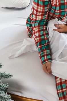 a person in pajamas sitting on a bed next to a small christmas tree and pillows