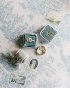 two wedding rings and some stamps on top of a blue tablecloth with white flowers