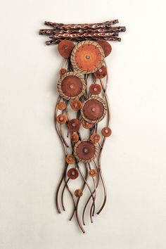 a metal wall hanging with wooden circles and leaves on it's sides, attached to a white wall