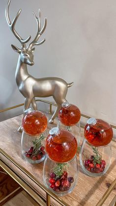 three vases filled with red berries sitting on top of a table next to a deer statue