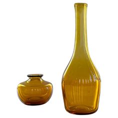 a yellow glass vase next to a brown glass bottle on a white background with a black lid