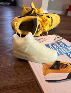 two pairs of yellow and black sneakers on top of a wooden floor next to a book