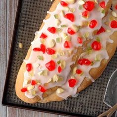 a pastry with white icing and cherries is on a baking sheet next to a spoon