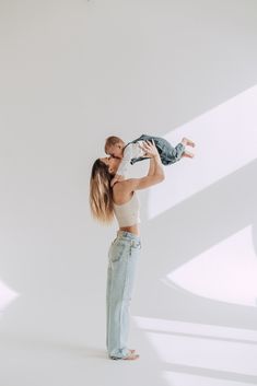 a woman holding a baby up to her face while standing in front of a white wall