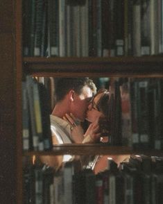 a man and woman kissing in front of a book shelf with many books on it