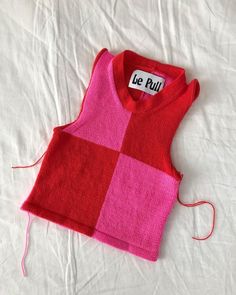 a pink and red sweater sitting on top of a white bed next to a string