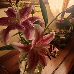 a vase filled with pink lilies on top of a wooden table next to a lamp