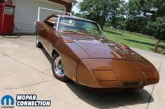 a brown sports car parked in front of a garage with an old fashioned gas pump