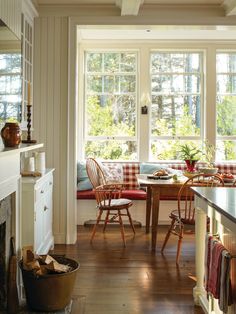 a kitchen table with chairs and a bench in front of two windows that look out onto the woods