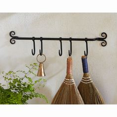 three brooms are hanging on the wall with two bells and one is holding a potted plant