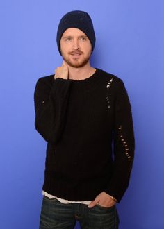 a man in a black sweater and hat posing for the camera with his hand on his chin