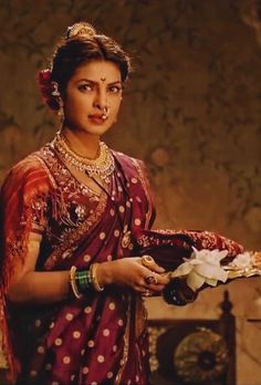 a woman in a red and white sari holding a vase with flowers on it