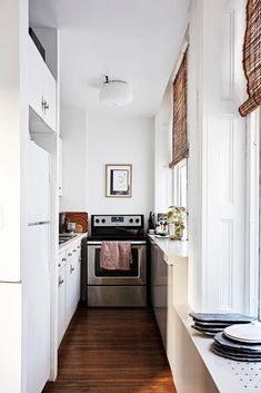 a long narrow kitchen with white cabinets and stainless steel appliances, along with wood flooring