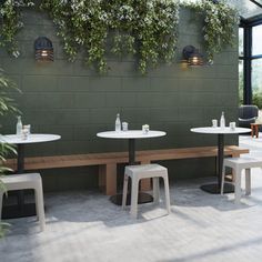 an outdoor seating area with tables and stools in front of a green wall filled with greenery