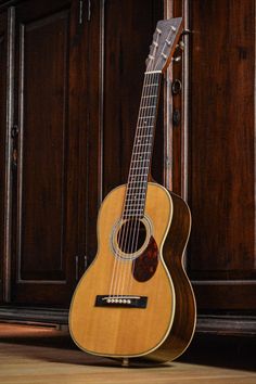 an acoustic guitar sitting on the floor in front of a wooden wall