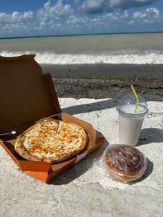 a pizza in a box next to a drink on the beach