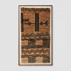 a brown and black rug hanging on a wall next to a wooden framed artwork piece