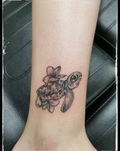 a small turtle tattoo on the ankle with flowers in it's center and an orange ribbon around its neck