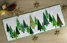 a quilted christmas tree table runner with green trees on it and gold ornaments around the edges