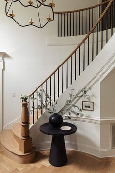 a black vase sitting on top of a wooden table next to a stair case in a house