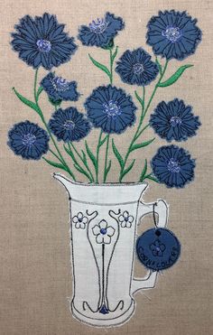 blue flowers are in a white vase on a beige background with an embroidered tag that says, i love you