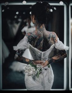 a woman in a wedding dress with tattoos on her back and arms, holding a bouquet