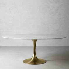 a white marble table with gold legs and an oval base, against a grey wall