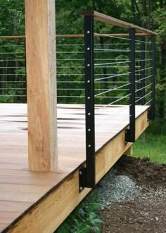 a wooden deck with metal railings in the middle of it and trees in the background