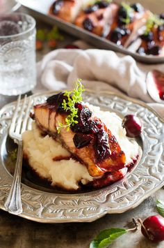 a plate topped with mashed potatoes and meat covered in cranberry sauce next to a glass of water