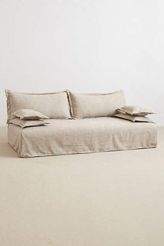 a couch with pillows on top of it in front of a white wall and floor