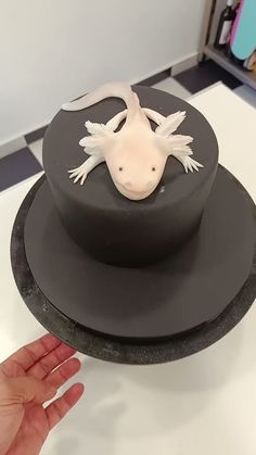 a cake shaped like a gecko on top of a black plate with a hand reaching for it