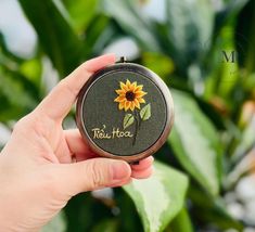 a person holding a small compact case with a sunflower on it and the word teatoo written in cursive writing