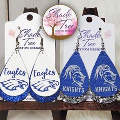 three pairs of blue and white earrings with the words eagle design on them are sitting on a wooden stand