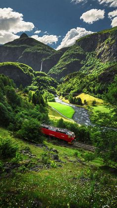 a red train traveling through a lush green valley