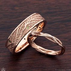 two gold wedding bands with green stones on them sitting on a wooden table next to each other