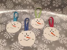 four snowman ornament hanging on a silver surface with snowflakes around them