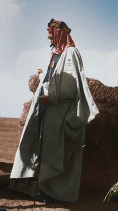 a man in an old photo wearing a long robe and headdress standing next to a pile of rocks