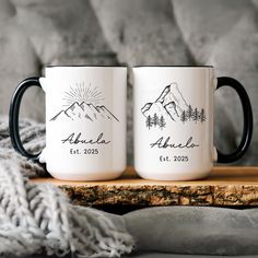 two black and white coffee mugs sitting on top of a wooden table next to a blanket