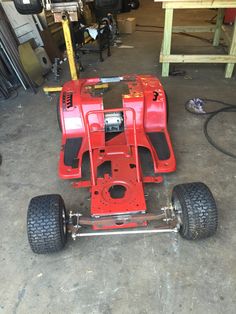 a red race car sitting on top of a floor in a garage next to some tools