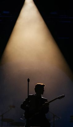 a man with a guitar standing in front of a microphone and spotlight on the stage