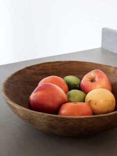 a wooden bowl filled with assorted fruit sitting on top of a counter next to a white wall