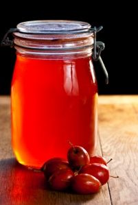 a jar filled with liquid sitting on top of a wooden table next to cherries