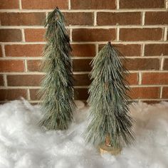 two small pine trees sitting on top of snow covered ground next to a brick wall