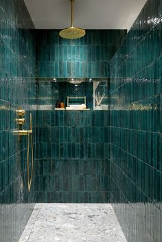 a green tiled bathroom with gold fixtures and blue tiles on the shower wall, along with an open shelf