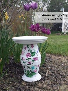 a white vase with flowers painted on it sitting in the grass next to some plants