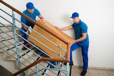 two men in blue uniforms moving boxes down the stairs