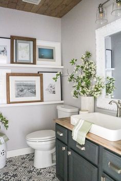 a white toilet sitting next to a sink in a bathroom under a wooden ceiling with framed pictures on the wall