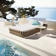 an outdoor lounge area next to a pool with water and trees in the back ground