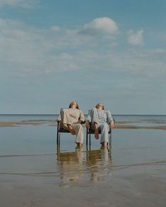 two people are sitting on chairs in the water at the beach and one person is laying down