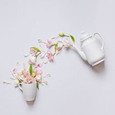 a white watering can filled with pink flowers next to a teapot on a table